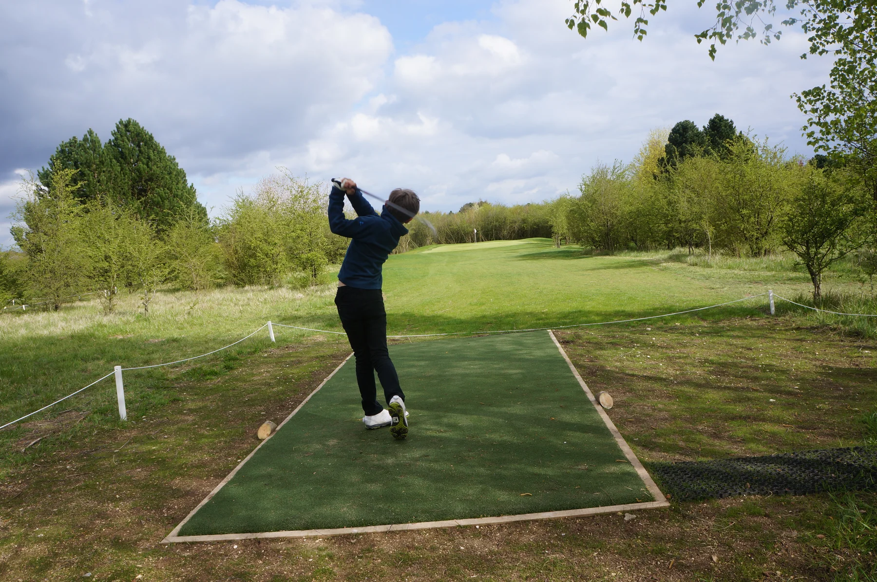 Golfer driving off an artificial turf tee box